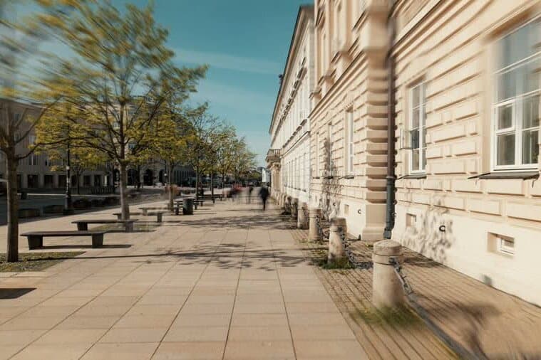 Pedestrians on a sunlit street lined with historic buildings