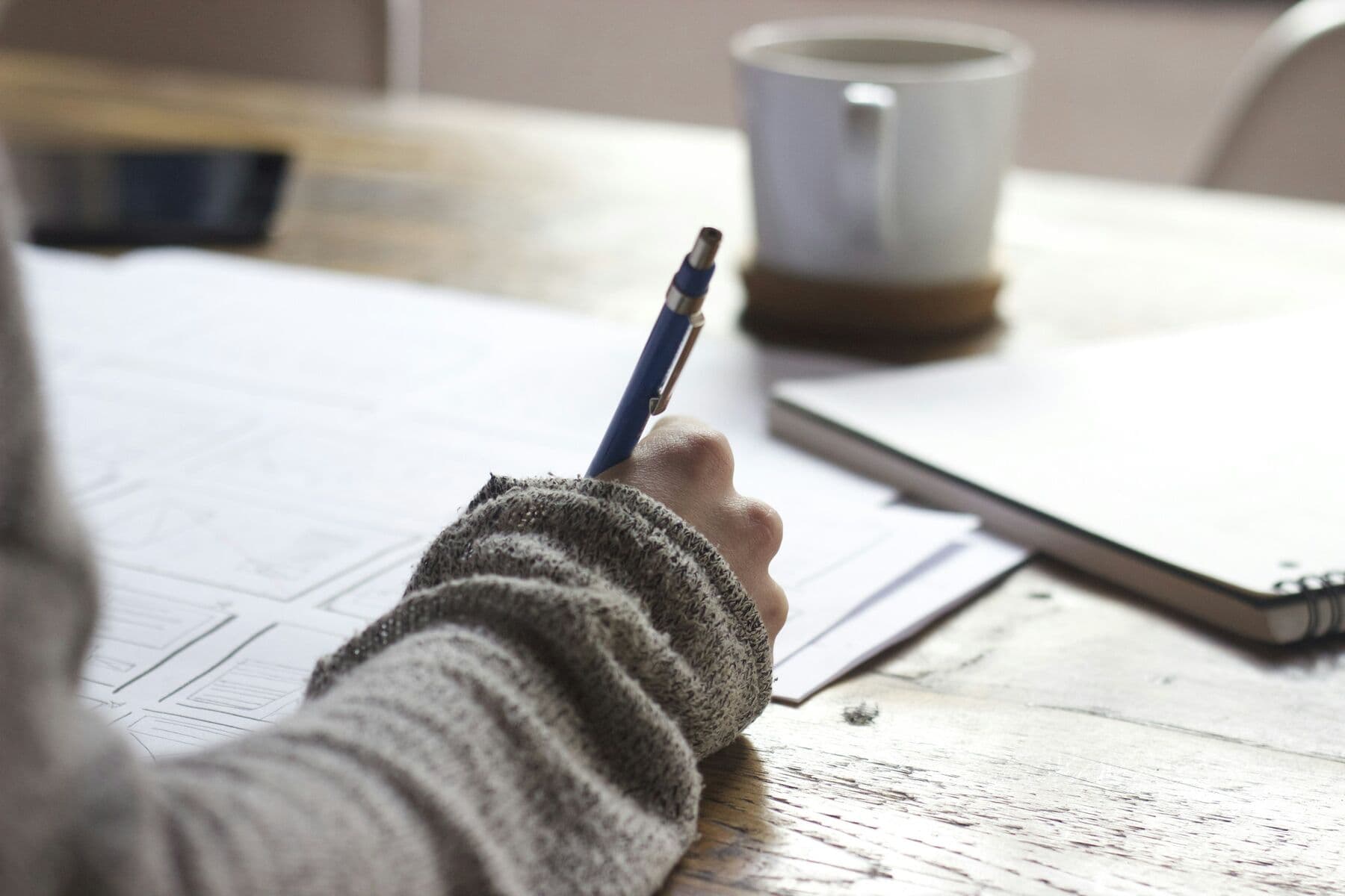 A hand writing notes on paper beside a coffee cup