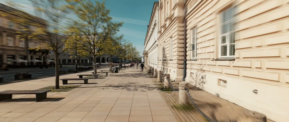 Pedestrians on a sunlit street lined with historic buildings